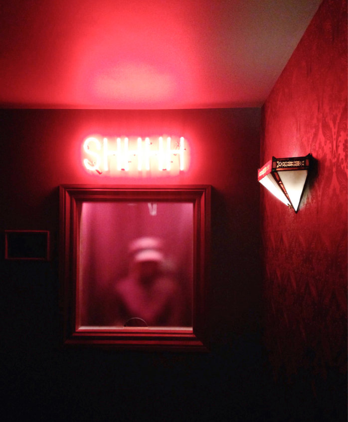 a dark room with a ticket window and a neon sign that says shhhh